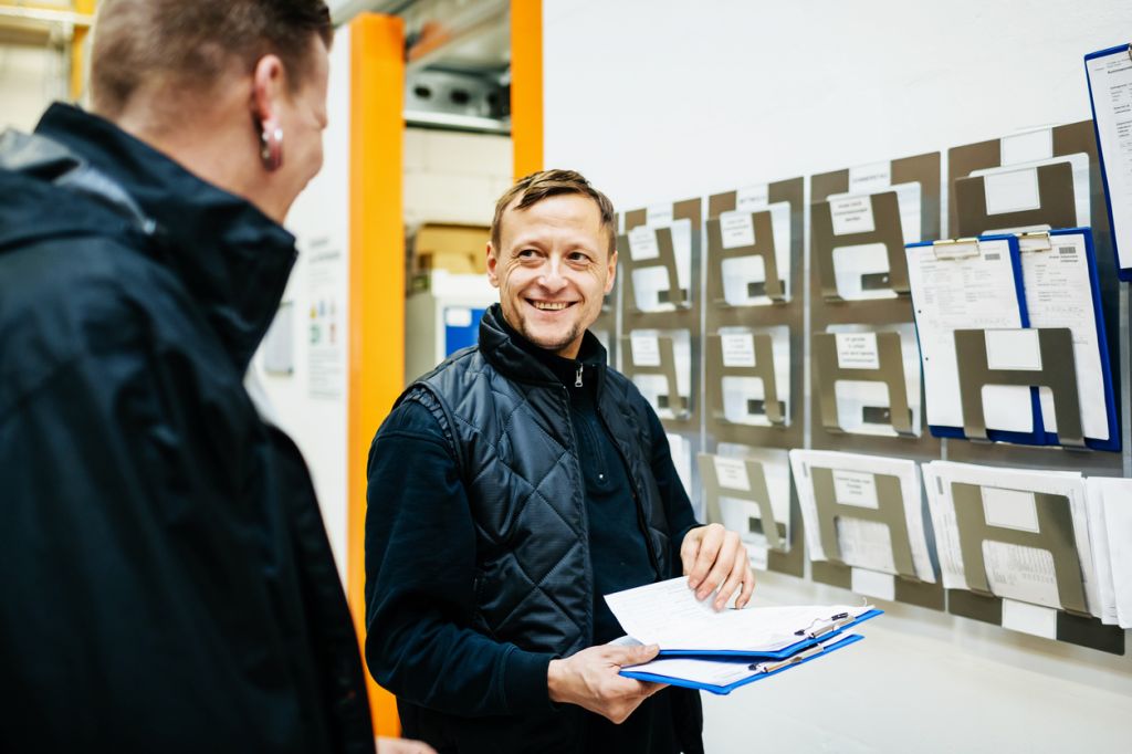 TommL – istockphoto.com A warehouse manager smiling as he chats to his colleague while organising their workload and schedule for the week.